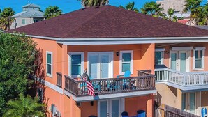 A two-story house with a red roof, a balcony with blue chairs, and an American flag.