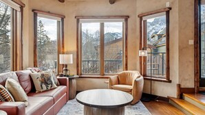 A cozy living room with a leather sofa, a round coffee table, and large windows offering mountain views.