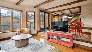 A spacious living room with a large flat-screen TV, wooden flooring, a round coffee table, and a red entertainment unit.