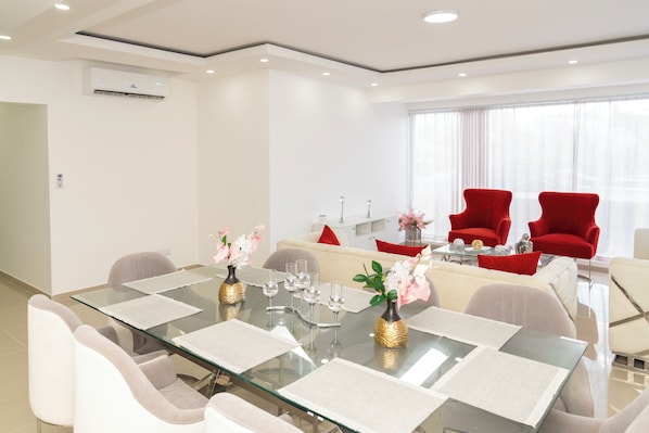 Un comedor moderno con una mesa de vidrio, sillas blancas y sillones rojos.