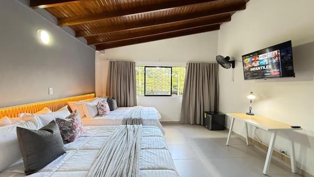Une chambre d’hôtel avec deux lits, un plafond en bois, un téléviseur fixé au mur et une fenêtre avec des rideaux.