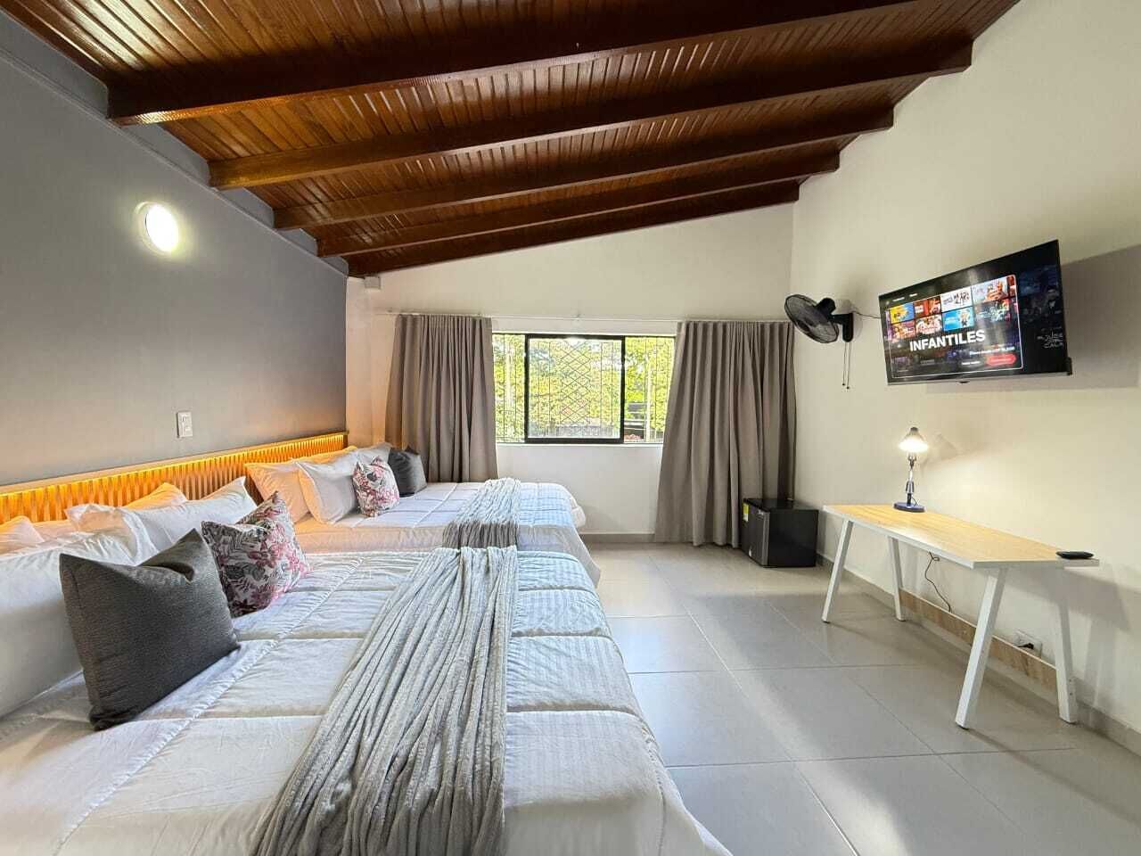 Una habitación con cama, escritorio, televisor y ventana.