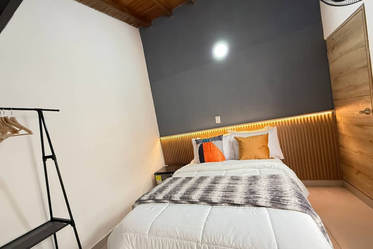 Un dormitorio con cama, cabecera de madera, mesita de noche y perchero.