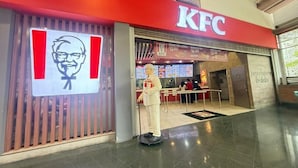 Un restaurant KFC avec un logo bien visible, un panneau affichant le menu et une statue d’un homme.