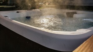 Ein Whirlpool mit aufsteigendem Dampf, vor einer Holzbalkendecke und einem Fenster mit Blick auf eine verschneite Landschaft.