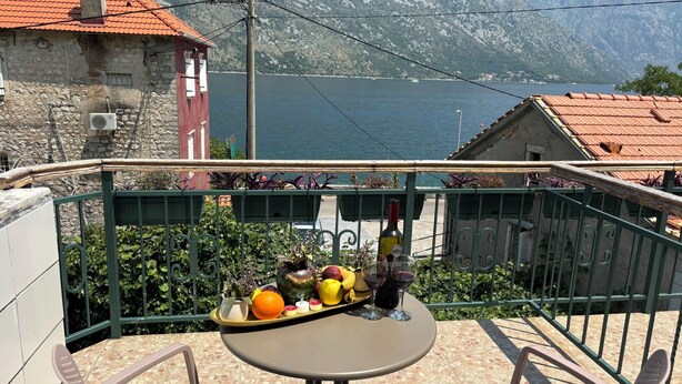 Eine Terrasse mit Tisch und Stühlen, eine Ablage mit Früchten und Weingläsern und Blick auf einen See und Berge.