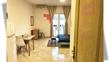 Una habitación pequeña y bien iluminada con cama, escritorio, silla y refrigerador.