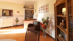 A living room with a sofa, a coffee table, a bookshelf, a dining area with a table and chairs, a kitchen in the background, and a mirror on the wall. - Vacation Home 'Sunrise Directly by the Sea' with Sea View, Private Terrace and Wi-Fi (La Mareta)