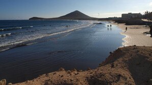 A beach with a mountain in the background, clear skies, and calm waters. - Vacation Home 'Sunrise Directly by the Sea' with Sea View, Private Terrace and Wi-Fi (La Mareta)