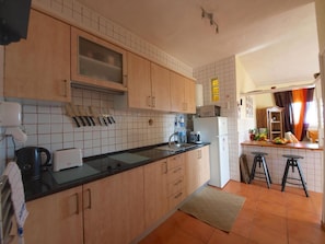 A kitchen with wooden cabinets, a black countertop, a microwave, a refrigerator, and a sink.