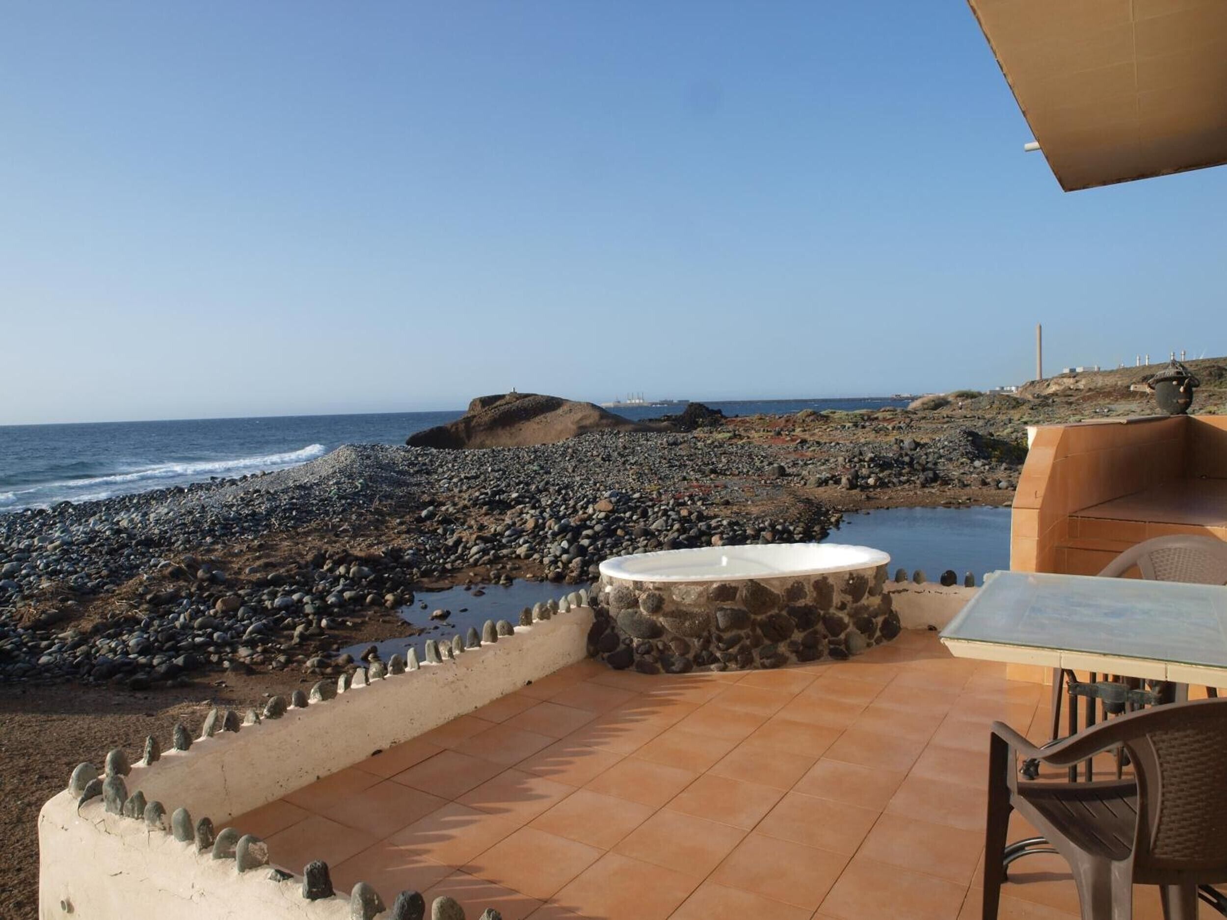 A patio with a stone table and chairs overlooking a rocky beach and ocean.
