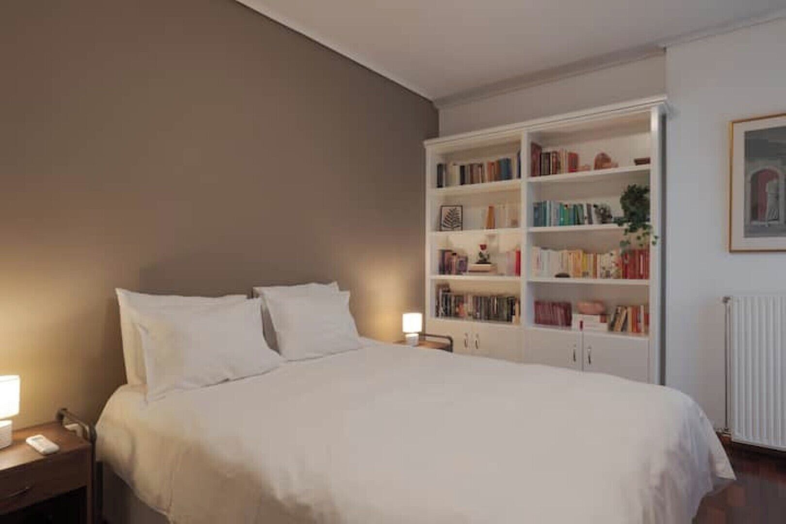 A bedroom with a large bed, a white bookshelf, and a nightstand with a lamp.
