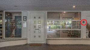 L’entrée d’un hôtel, avec une porte blanche, une fenêtre en verre ornée d’un sapin de Noël et une enseigne sur laquelle on peut lire « DRAGITAI ».