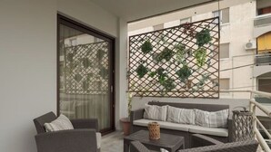 Un balcon doté de meubles en osier, d’une porte-fenêtre coulissante et d’une treille ornée de plantes.
