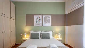A hotel room with a bed, two bedside lamps, a wall-mounted air conditioner, and a set of towels on the bed. - Best view of Acropolis - Modern 2BR Apt by Meros (Athina)