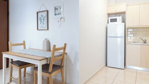A small kitchen with a refrigerator, microwave, and wooden cabinets. There is a dining table with chairs and a framed picture on the wall. - Best view of Acropolis - Modern 2BR Apt by Meros (Athina)