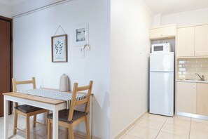 A small kitchen with a refrigerator, microwave, and wooden cabinets. There is a dining table with chairs and a framed picture on the wall. - Best view of Acropolis - Modern 2BR Apt by Meros (Athina)