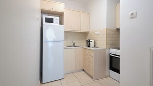 A compact kitchen with a refrigerator, microwave, oven, and a small countertop. - Best view of Acropolis - Modern 2BR Apt by Meros (Athina)