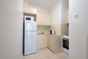 A compact kitchen with a refrigerator, microwave, oven, and a small countertop. - Best view of Acropolis - Modern 2BR Apt by Meros (Athina)