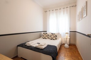A neatly made bed with a black and white quilt, a bedside lamp, and a window with curtains.