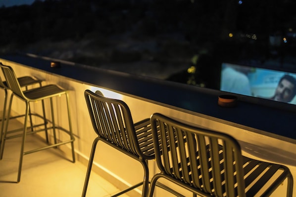 A bar area with metal chairs and a television screen displaying a person.