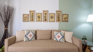 A beige sofa with patterned cushions, a wall with framed floral artwork, and a tall vase of branches. - Best view of Acropolis - Modern 2BR Apt by Meros (Athina)