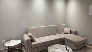 A modern living room with a beige sectional sofa, a small round table, and a coffee table. - Charming 1-bedroom apartment in the heart of welcoming Agia Napa with AC (Ayia Napa)