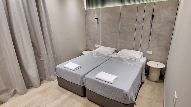 A modern bedroom with two beds, a round side table, and a headboard with vertical lines. - Charming 1-bedroom apartment in the heart of welcoming Agia Napa with AC (Ayia Napa)