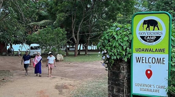 A sign welcoming visitors to Governor's Camp in Udawalawe, Sri Lanka, with a backdrop of lush greenery and a dirt path.