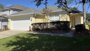 A residential house with a garage, a well-maintained lawn, and a tree in the foreground. - Peaceful Lake Berkley Retreat (Kissimmee)