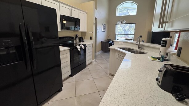 A modern kitchen with a black refrigerator, white cabinets, a microwave, and a sink. - Peaceful Lake Berkley Retreat (Kissimmee)