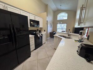 A modern kitchen with a black refrigerator, white cabinets, a microwave, and a sink.