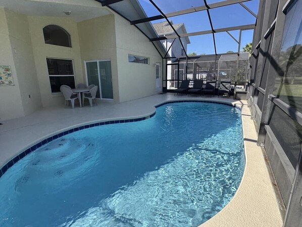 An indoor swimming pool with a glass ceiling, a covered patio area, and a seating arrangement.