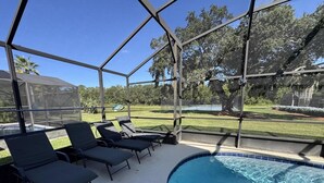 A covered outdoor swimming pool with lounge chairs and a view of the surrounding landscape. - Peaceful Lake Berkley Retreat (Kissimmee)