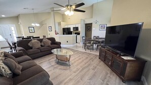 A living room with a sofa, coffee table, TV, and a kitchen in the background. - Peaceful Lake Berkley Retreat (Kissimmee)