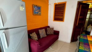 Un espace de vie compact comprenant un canapé, un réfrigérateur et une table aux couleurs vives.