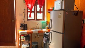 Une cuisine compacte équipée d’un réfrigérateur, d’une cuisinière, d’un évier et d’une fenêtre ornée de rideaux rouges.