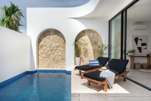 Un área de piscina moderna con dos sillones reclinables, una pared de piedra y un ventanal que da a una habitación.