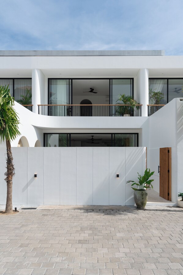 Una casa moderna de dos pisos con techo plano, ventanas amplias y un balcón.