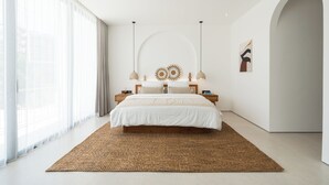 A modern bedroom with a large bed, a ceiling fan, and a view of the outdoors through large windows.