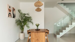 A modern dining area with a wooden table, two hanging wicker lamps, a potted plant, and abstract wall art.
