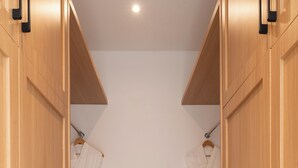 A modern walk-in closet with wooden doors and black handles, featuring two white robes hanging on racks.