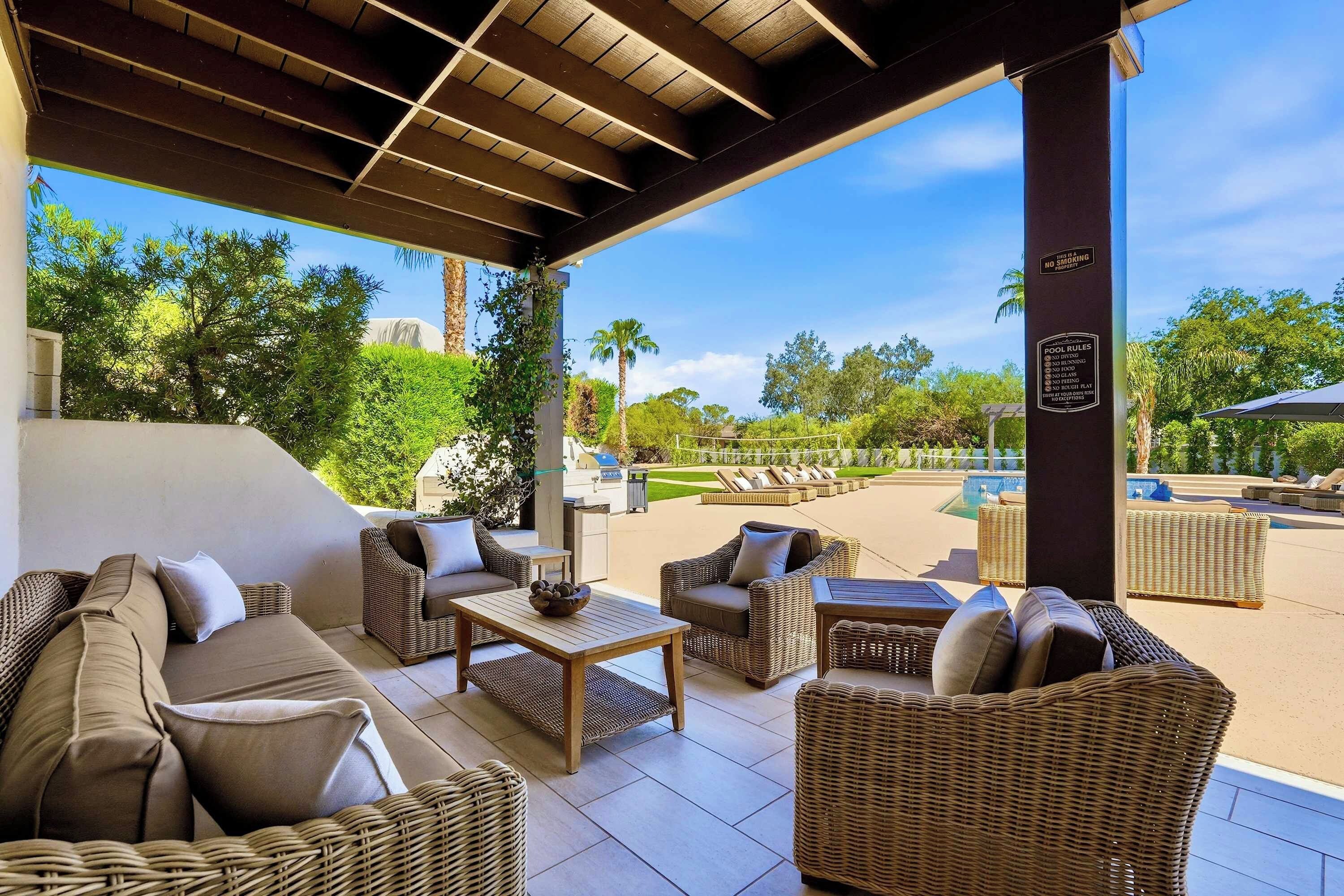 A covered outdoor seating area with wicker furniture and a view of a pool and greenery.