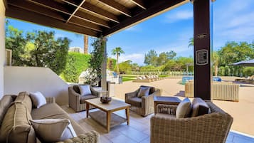 A covered outdoor seating area with wicker furniture and a view of a pool and greenery.