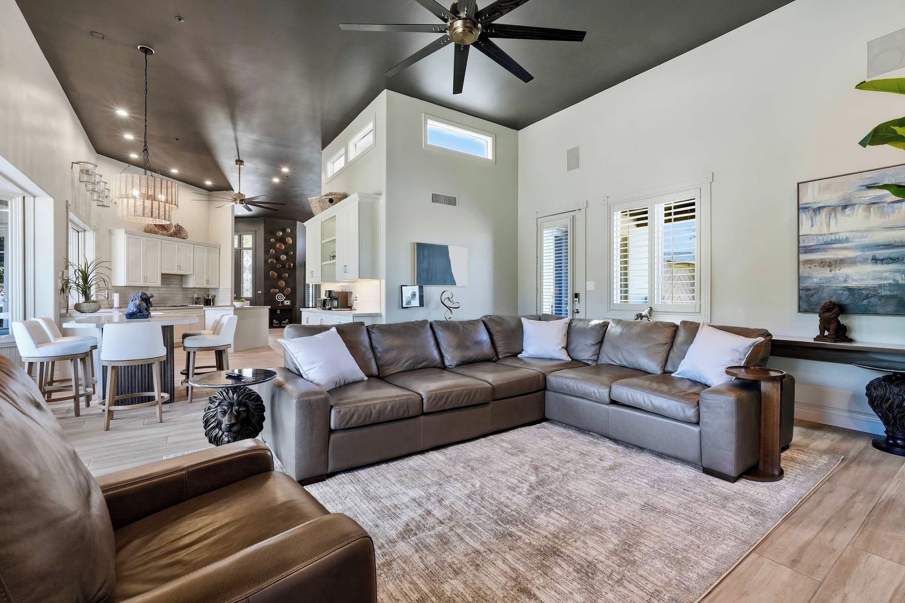 A spacious living area with a large sectional sofa, a dining area with a kitchen in the background, and a ceiling fan.