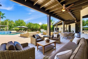 A covered outdoor seating area with wicker furniture, a pool, and a view of the surrounding greenery.