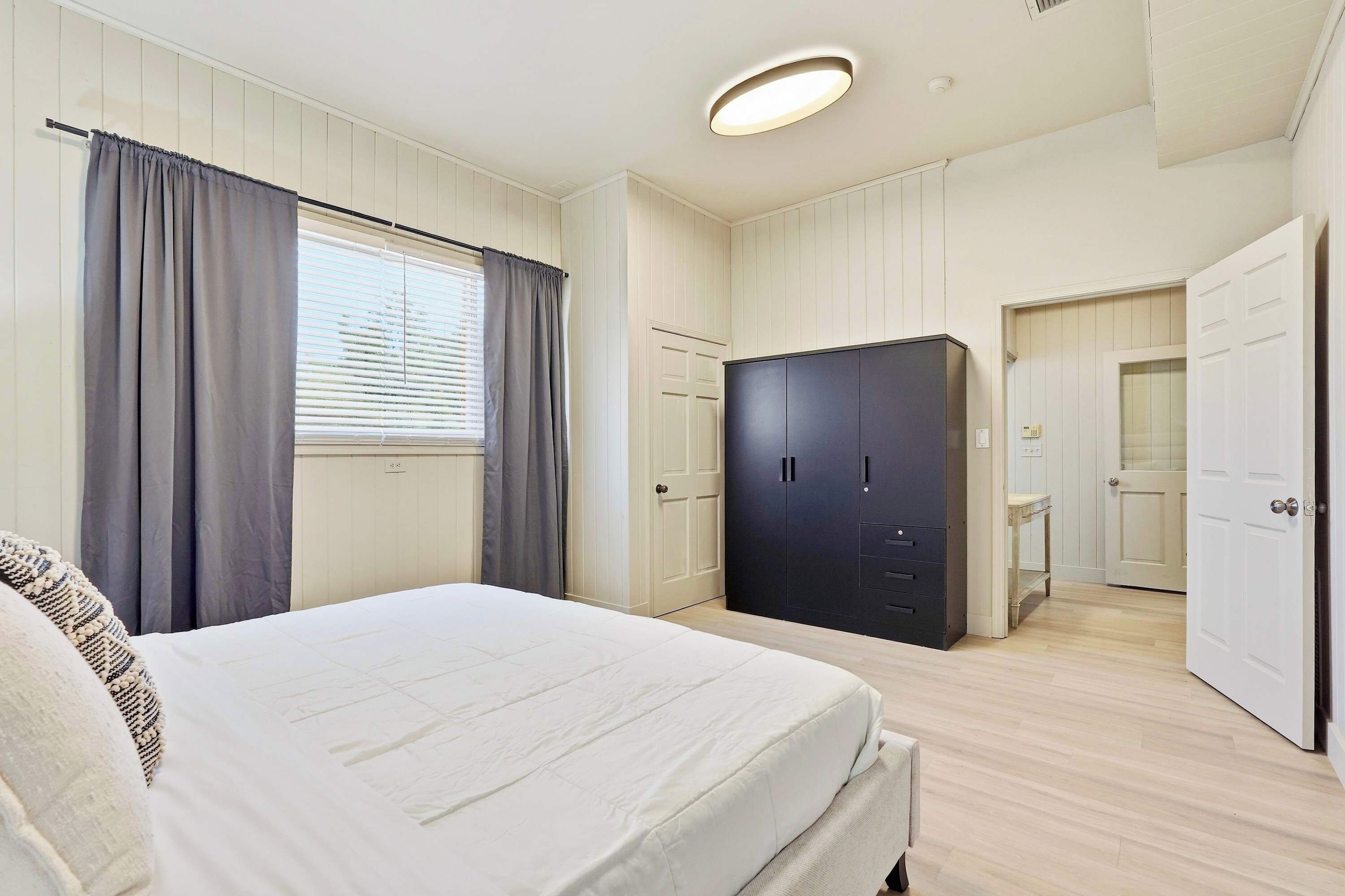 Une chambre à coucher avec un lit, une armoire et une salle de bain visible à travers une porte ouverte.