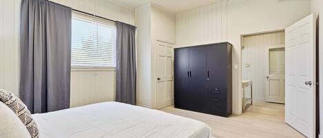 Une chambre à coucher avec un lit, une armoire et une salle de bain visible à travers une porte ouverte.