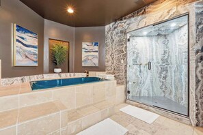 A modern bathroom with a marble shower enclosure, a bathtub, and artwork on the walls.