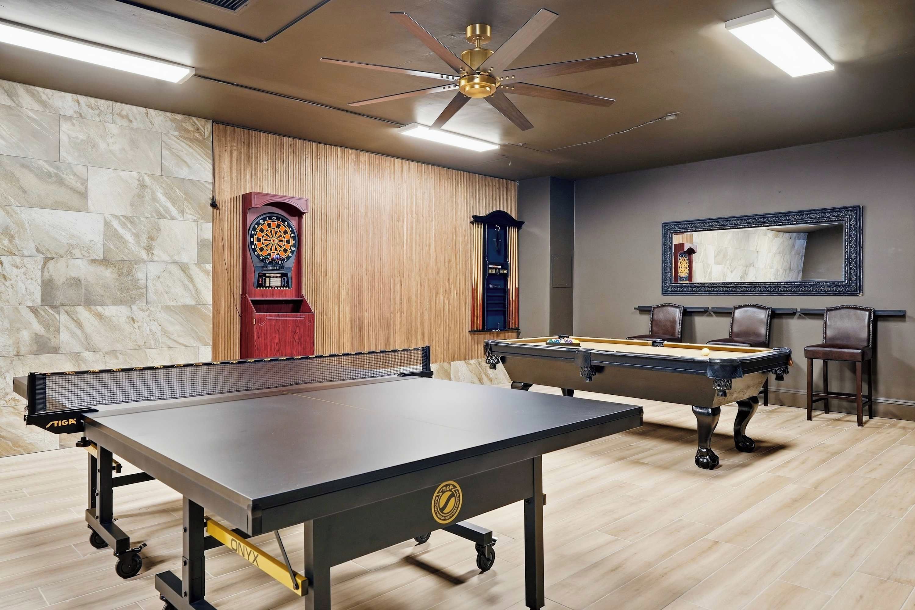 A billiards room with a pool table, another pool table, a dartboard, and a ceiling fan.